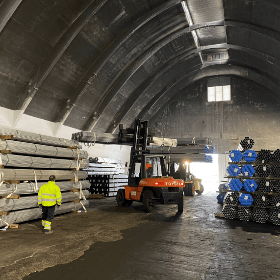 Magazzino industriale con tubi metallici impilati e muletto